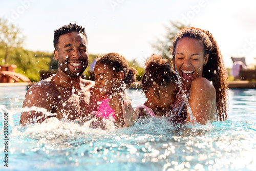 Family On Summer Holiday With Two Girls Being Held In Swimming Pool By Parents And Splashing photo