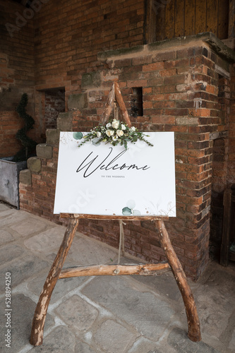 Welcome sign to wedding, wooden frame natural wood with flowers bouquet floral display.  Standing outside wedding venue to welcome guests.
