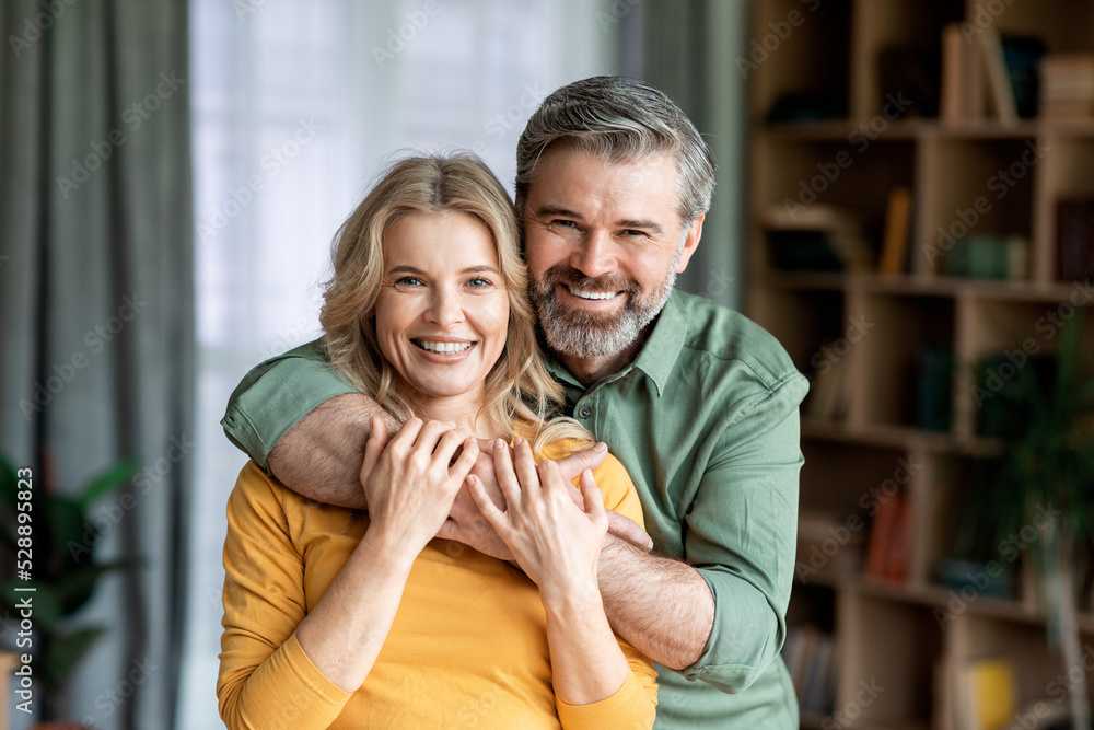 Portrait Of Loving Middle Aged Spouses Embracing And Smiling At Camera