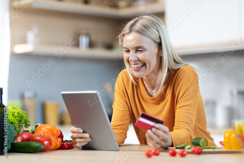 Happy blonde woman buying food online  using digital pad