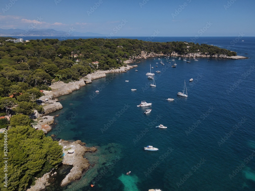 Naklejka premium Aerial view of Cap d'Antibes and Billionaire's Bay. Beautiful rocky beach near coastal path on the Cap d'Antibes, Antibes, France. Drone view from above of Côte d’Azur near Juan-les-Pins and Cannes.
