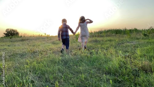 Silhouette little kids walking skipping on meadow forward golden lights of summer sunset. Cheerful girl, cute boy having fun at countryside. Lovely children enjoying pastime at nature. Simple living