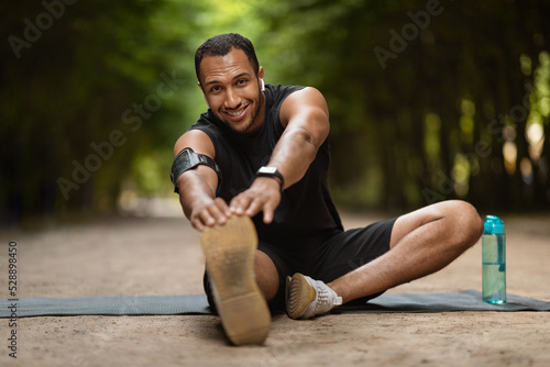 Fototapeta Naklejka Na Ścianę i Meble -  Positive muscular black man stretching in the park