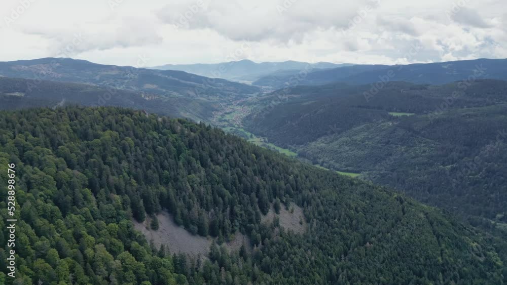 Aerial drone view of the mountain, the valley, the forest and the low clouds below the Vosges Schlucht pass, with the village of Munster in the distance, by gray cloudy weather Aerial drone view of the mountain, the valley, the forest and the low clouds below the Vosges Schlucht pass, with the village of Munster in the distance, by gray cloudy weather