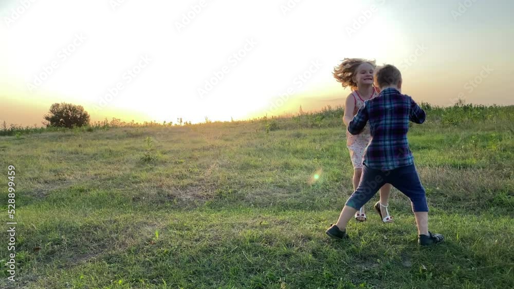 Cheerful kids having fun at meadow, swirling by holding hands, laughing in golden lights of summer sunset. Beautiful girl and cute boy playing together outdoors. Happiness in simple living Cheerful kids having fun at meadow, swirling by holding hands, laughing in golden lights of summer sunset. Beautiful girl and cute boy playing together outdoors. Happiness in simple living