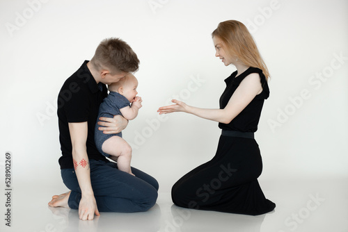 Portrait of young beautiful family in dark clothes with plump cherubic baby infant toddler sitting on white background.
