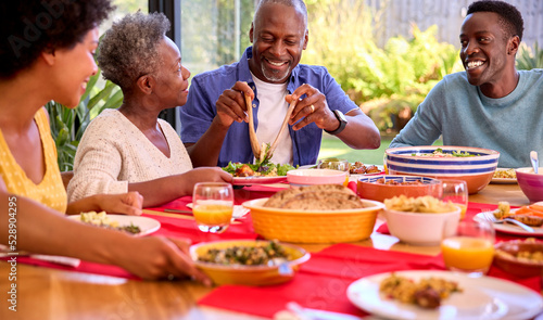 Parents With Adult Offspring Sitting Around Table At Home Enjoying Meal Together