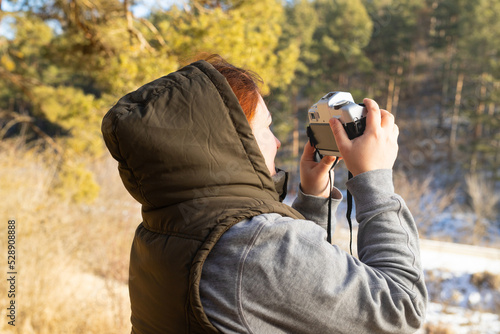 Traveler woman photographer standing in front of the forest on winter sunny day taking photo using camera.