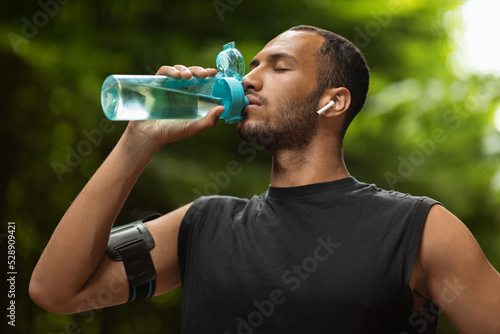 Athletic black man drinking water, training at park