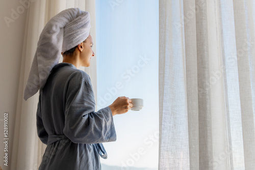 Relaxed woman wearing bath robe drinking coffee in hotel room in morning