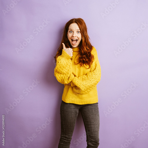 enthusiastic redhead woman shows a thumbs up, copyspace with purple background photo