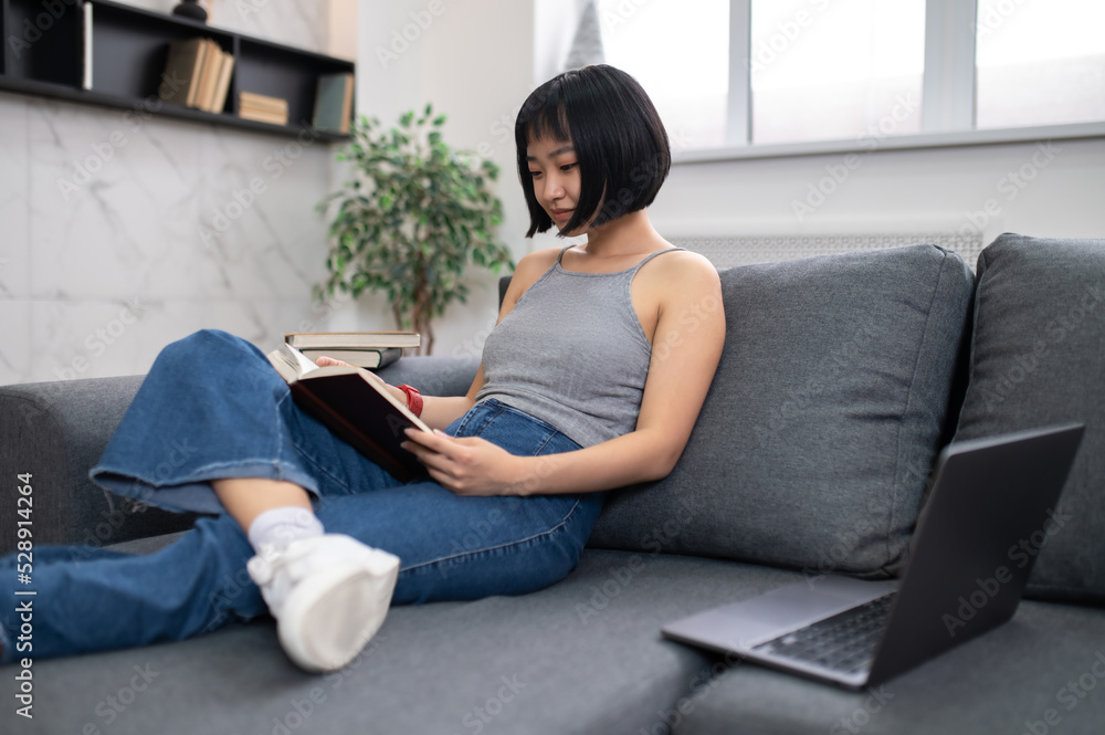 A short-haired young woman reading a book while sitting on the sofa A short-haired young woman reading a book while sitting on the sofa
