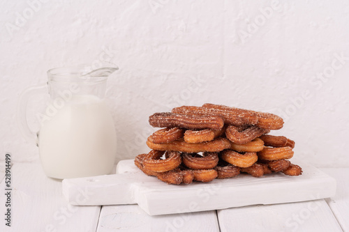 Homemade churros with milk and cream on a white wooden background.