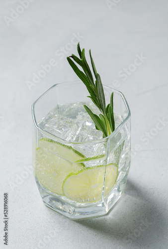 Classic Gin and tonic or Tom Collins or Gin Fizz alcoholic cocktail with Gin, tonic, ice, lime and rosemary on a grey background