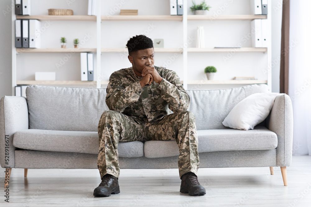 Pensive african american soldier in military uniform sitting on couch