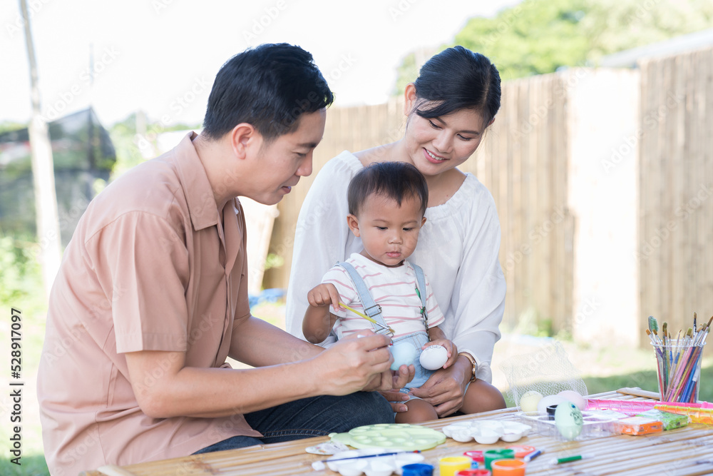 Asian family with baby little son painting eggs with brush in class workshop. Happy Asian father and mother with little son and teaching painting eggs with water colour