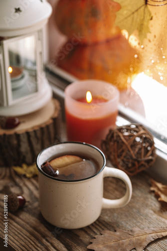  Mug of hot tea with apple and cinnamon on the autumn window. Autumn and fall cozy vertical postcard 