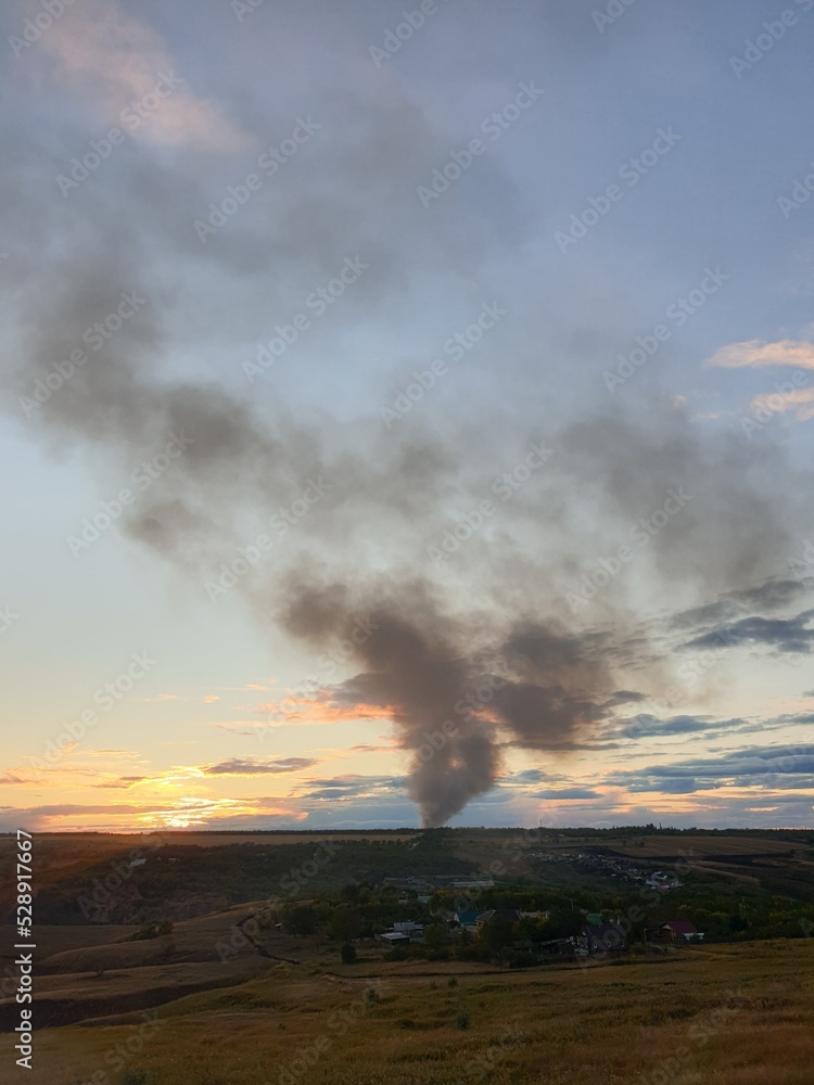 black smoke from the fire on the background of the sunset sky.