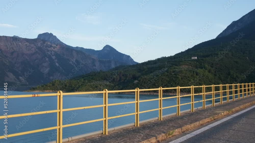 Panning shot of bridge passing over lake with scenic view on mountains during sunset. Panning shot of bridge passing over lake with scenic view on mountains during sunset.