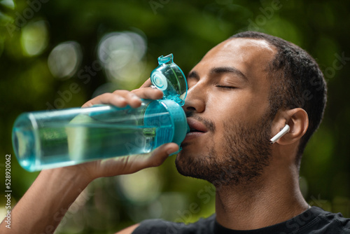 Sporty african american man drinking water, training at park