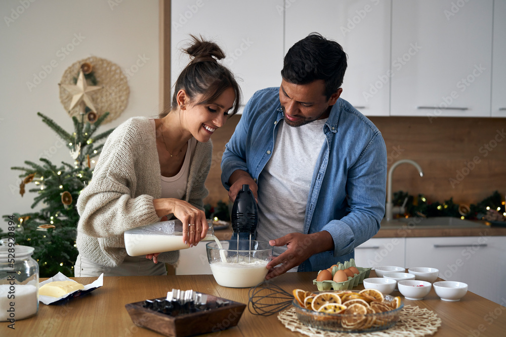 Multi ethnicity couple making a cake together in Christmas time Multi ethnicity couple making a cake together in Christmas time