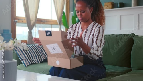 Young upset African American woman remains dissatisfied after receiving online order experiences bad emotions putting box on table sits on sofa in living room. Negative shopping experience photo