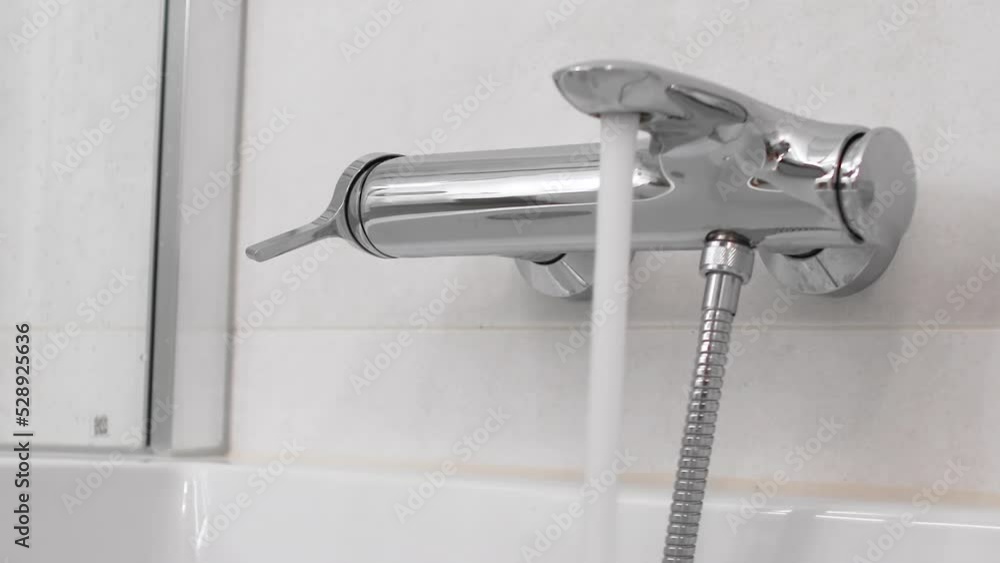 Caucasian hand opening a shiny metal bathtub faucet in a luxurious bathroom Caucasian hand opening a shiny metal bathtub faucet in a luxurious bathroom