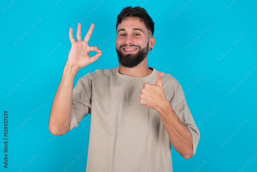 bearded caucasian man wearing casual T-shirt over blue background smiling and looking happy, carefree and positive, gesturing victory or peace with one hand bearded caucasian man wearing casual T-shirt over blue background smiling and looking happy, carefree and positive, gesturing victory or peace with one hand