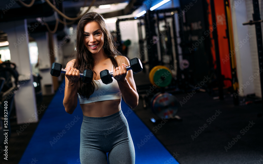 Fototapeta premium Young fit beautiful woman doing exercises with dumbbell in fitness club.