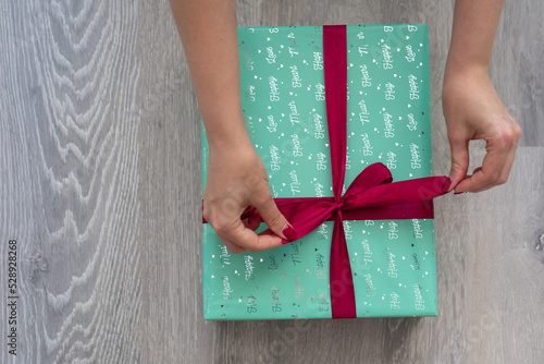 woman hand holding green turquoise color gift box with red ribbon bow on grey wooden background. Concept: holiday, celebration, birthday, New Year, Christmas, Valentines Day, Mothers Day, Thanksgiving