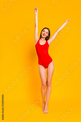 Vertical full length photo of adorable sweet lady dressed bodysuit walking rising arms isolated yellow color background