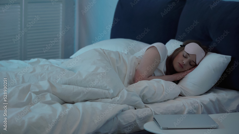 Woman in mask sleeping on bed near laptop on bedside table. Woman in mask sleeping on bed near laptop on bedside table.
