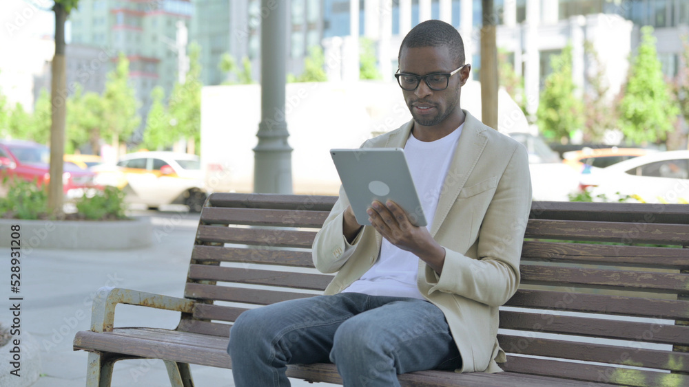 Fototapeta premium African Man using Tablet while Sitting Outdoor on Bench