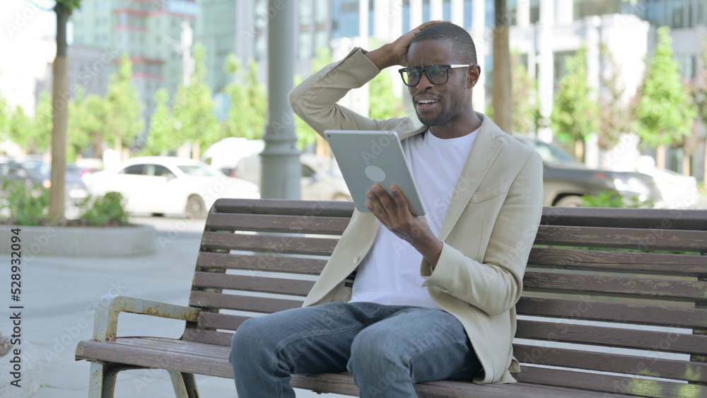 Upset African Man Reacting to Loss on Tablet while Sitting Outdoor on Bench Upset African Man Reacting to Loss on Tablet while Sitting Outdoor on Bench