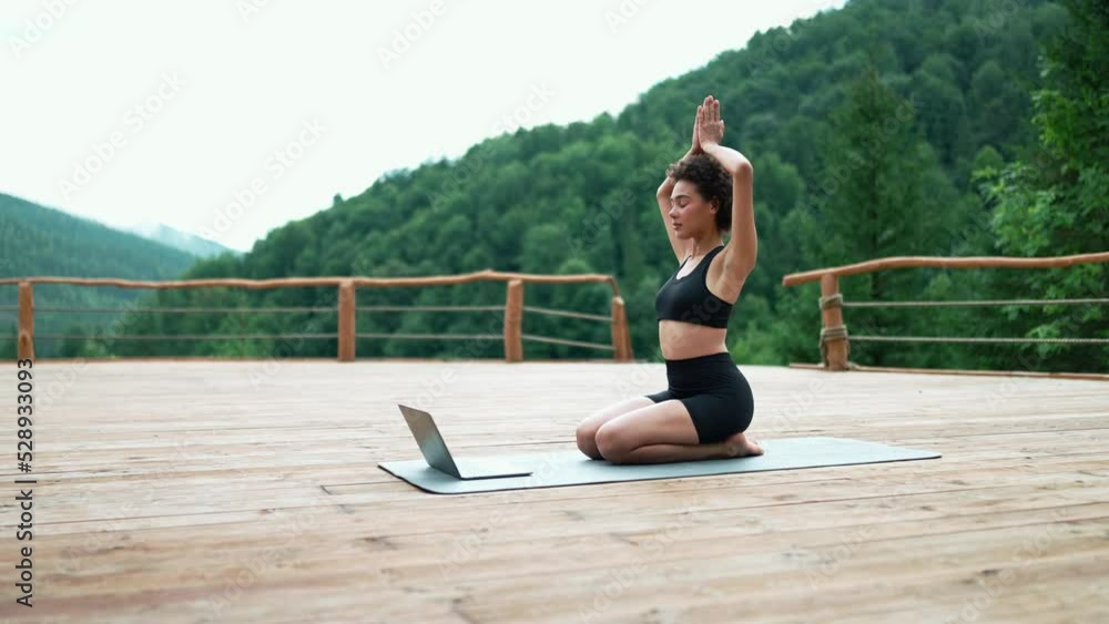 Confident African sporty woman doing meditation with online lesson on laptop in the mountains outdoors Confident African sporty woman doing meditation with online lesson on laptop in the mountains outdoors