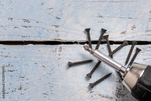 black screws and a the top of s cordless screwdriver on a wooden blue background with copy space