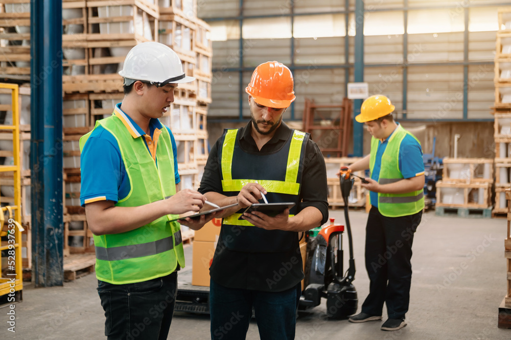 Management having discussion at warehouse with white hardhat using digital tablet Working in Logistics and Distribution Center.. Management having discussion at warehouse with white hardhat using digital tablet Working in Logistics and Distribution Center..