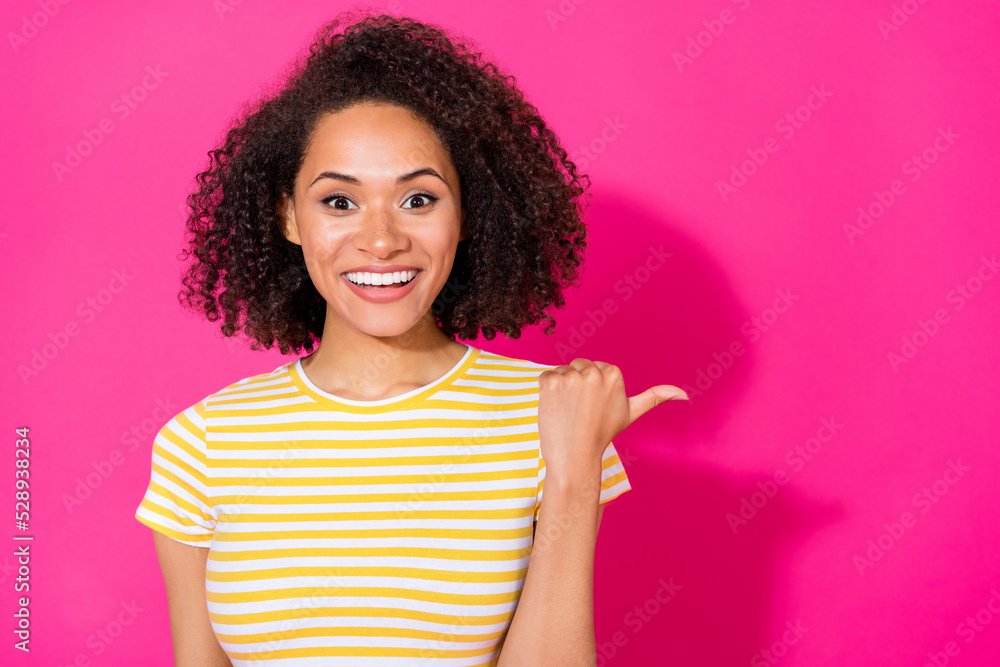 Photo of young pretty cute nice woman wear striped yellow t-shirt finger pointing empty space excited isolated on pink color background Photo of young pretty cute nice woman wear striped yellow t-shirt finger pointing empty space excited isolated on pink color background