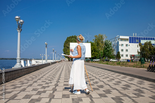 White canvas on a wooden tripod. A woman artist paints a city landscape. © Andrey_Arkusha