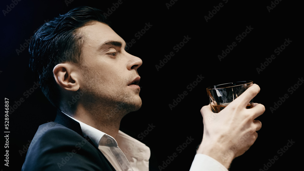Side view of businessman in suit holding glass of whiskey isolated on black. Side view of businessman in suit holding glass of whiskey isolated on black.