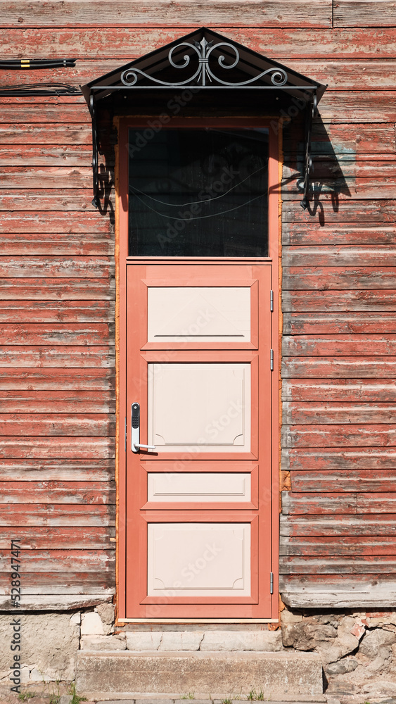 Old red wooden doors, entrance to wooden house with withered peeling brown paint on the walls. Tartu, Estonia. European historic architectural details.
