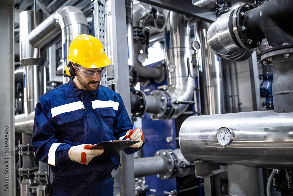 Professional worker in protective uniform and hardhat standing by pipes and checking pressure inside gasoline refinery plant. Professional worker in protective uniform and hardhat standing by pipes and checking pressure inside gasoline refinery plant.