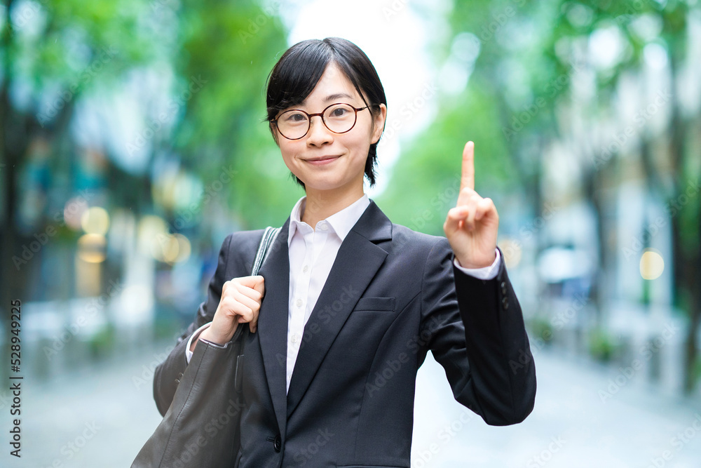 人差し指を上げたポーズをするスーツ姿の若い女性 人差し指を上げたポーズをするスーツ姿の若い女性
