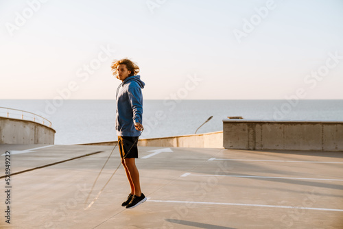 Young blonde man working out with jumping rope on parking