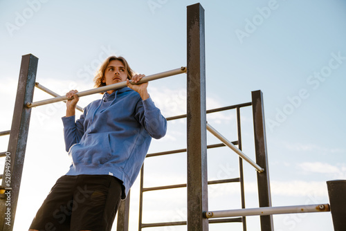 Young blonde man doing exercise while working out on horizontal bar