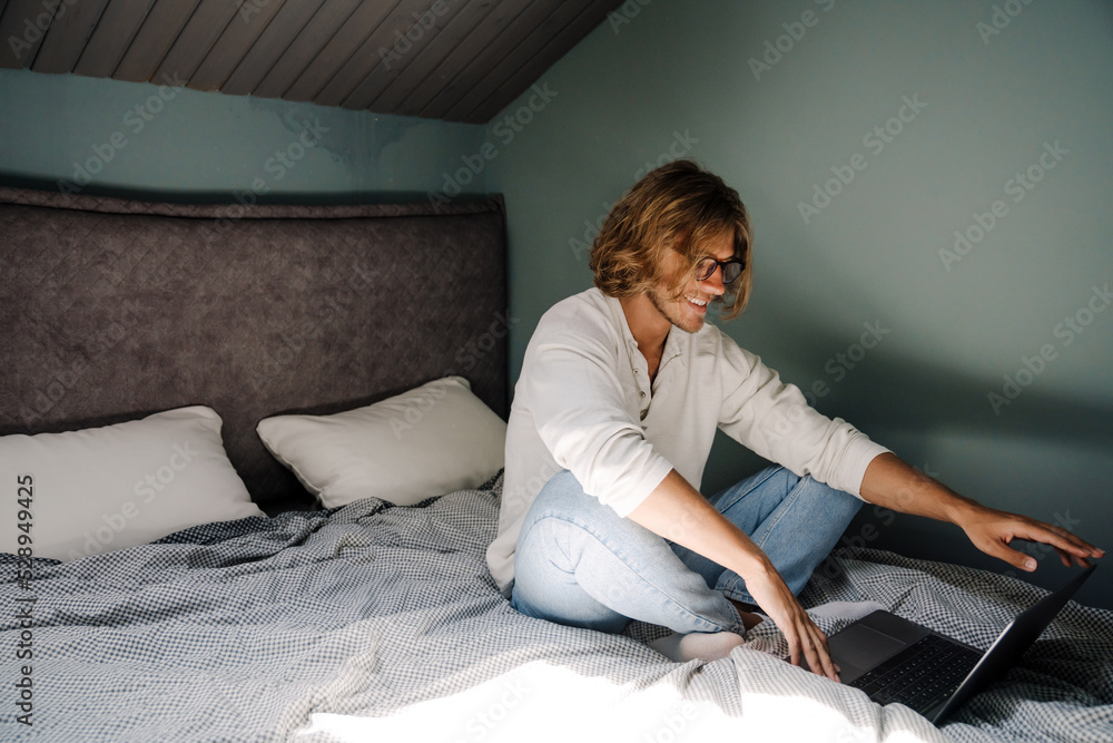 Blonde bristle man working with laptop while sitting on bed at home