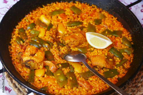 spanish paella close up photo in frying pan with shrimps, peas and lemon slice