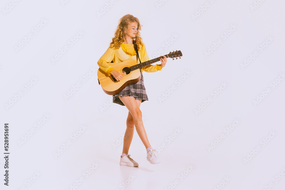 Portrait of beautiful young girl on yellow blouse and checkered skirt playing guitar isolated over grey background Portrait of beautiful young girl on yellow blouse and checkered skirt playing guitar isolated over grey background
