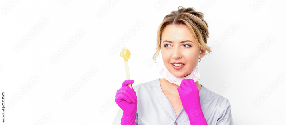 The master of sugar hair removal holds liquid yellow sugar paste, wax for depilation on a wooden stick on a white background The master of sugar hair removal holds liquid yellow sugar paste, wax for depilation on a wooden stick on a white background