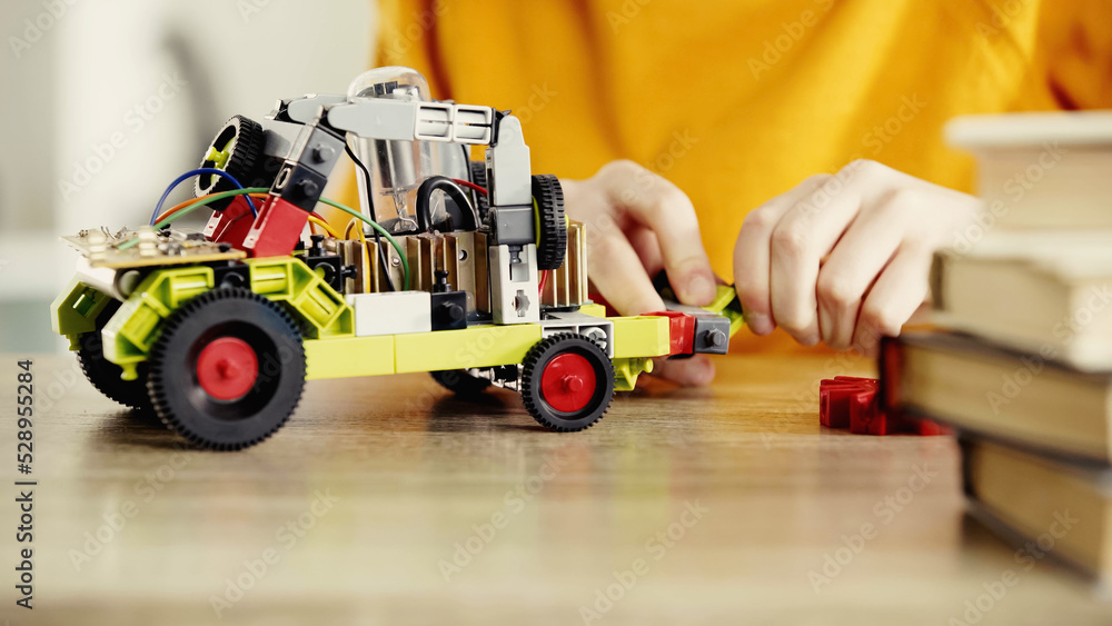 cropped view of child playing with electric car made of building blocks on table near books. cropped view of child playing with electric car made of building blocks on table near books.